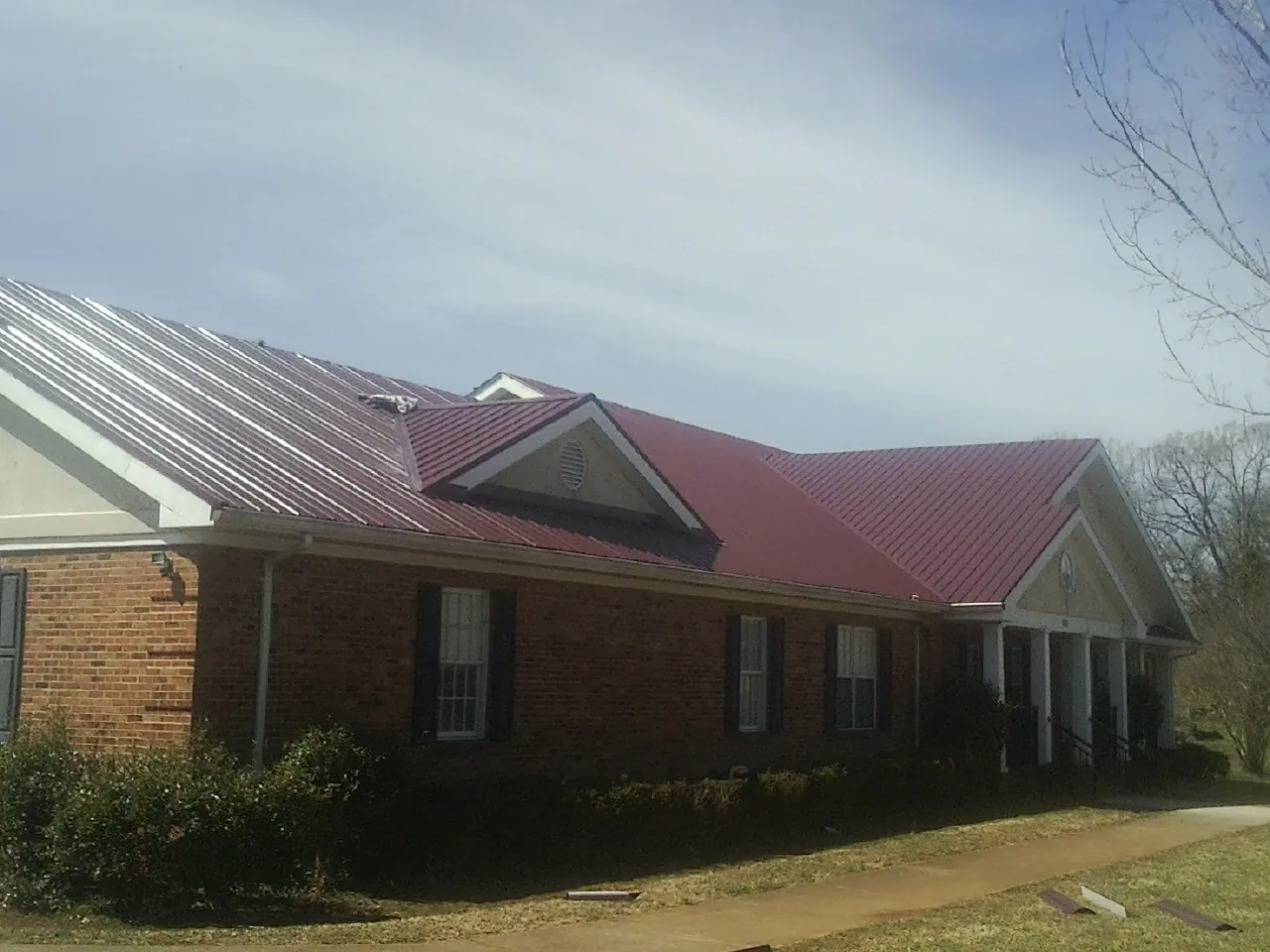 Red metal roof with gabled entries on a long brick building, from a Hail Damage Roof Repair job in Casa Grande